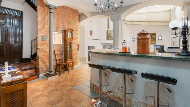 Una cocina con pared de ladrillo, puerta de madera, un reloj y una barra con taburetes.