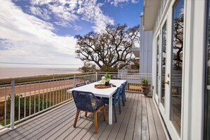 A deck with a table and chairs, a railing, and a view of the beach. - New Luxury Beach Home - Heated Pool + Pickleball! (Pass Christian)