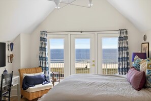 A bedroom with a large bed, a chair, a small table, and a view of the ocean through a balcony door. - New Luxury Beach Home - Heated Pool + Pickleball! (Pass Christian)