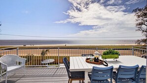 Une terrasse avec une table et des chaises, un banc en osier blanc et un jardinier agrémenté de plantes vertes.