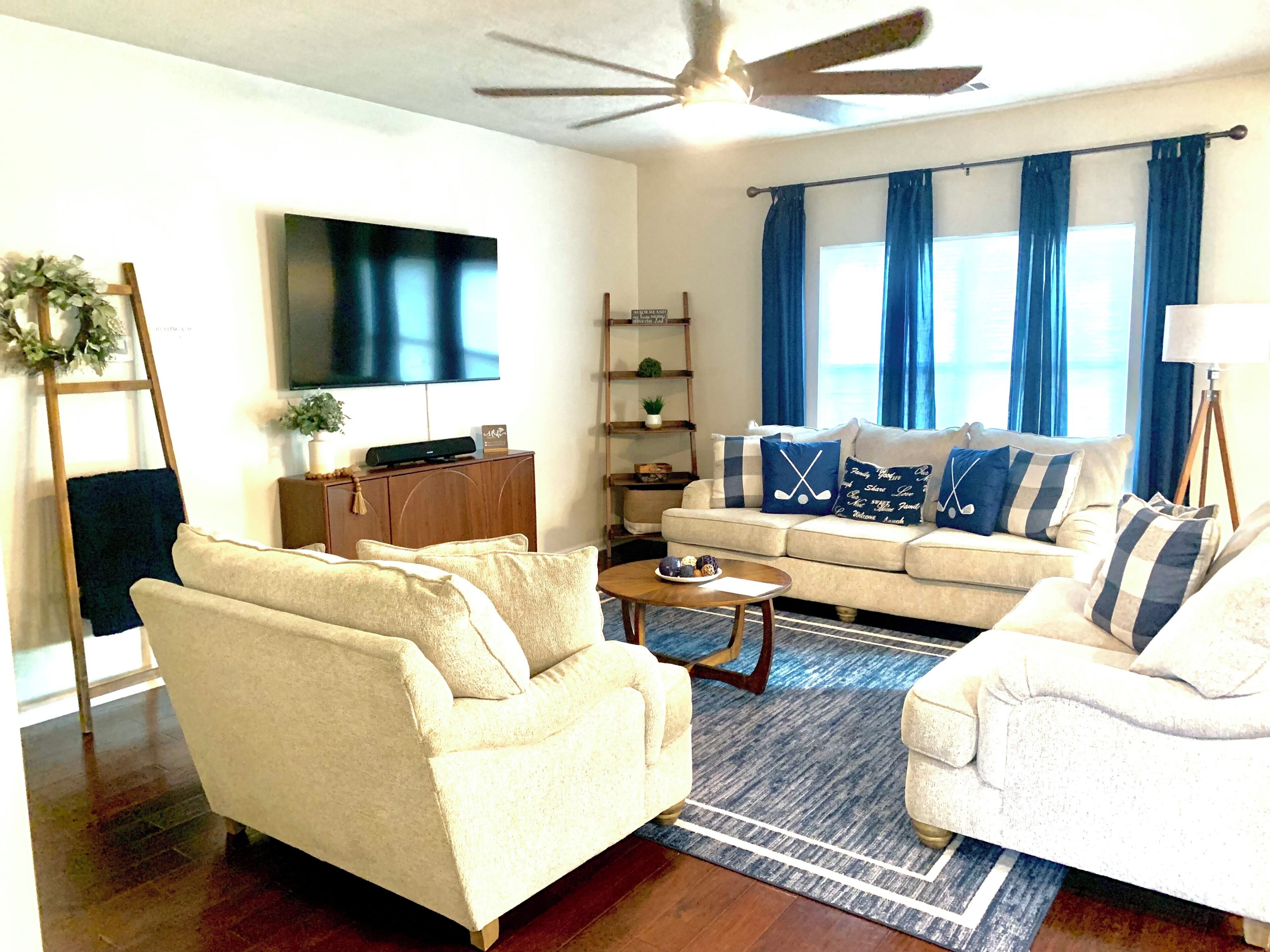 A living room with a sofa set, a coffee table, a TV, a ceiling fan, and a window with curtains.
