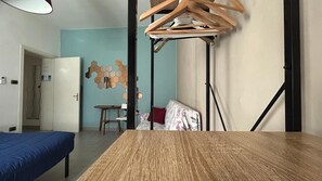 A room with a wooden table, a bed with a blue cover, a hanging clothes rack, and a wall with hexagonal tiles. - Ankon Apartments La Casa Di Joye & Nemi (Ancona)