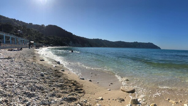 Une plage avec une eau claire, des galets et un bâtiment situé sur la gauche.