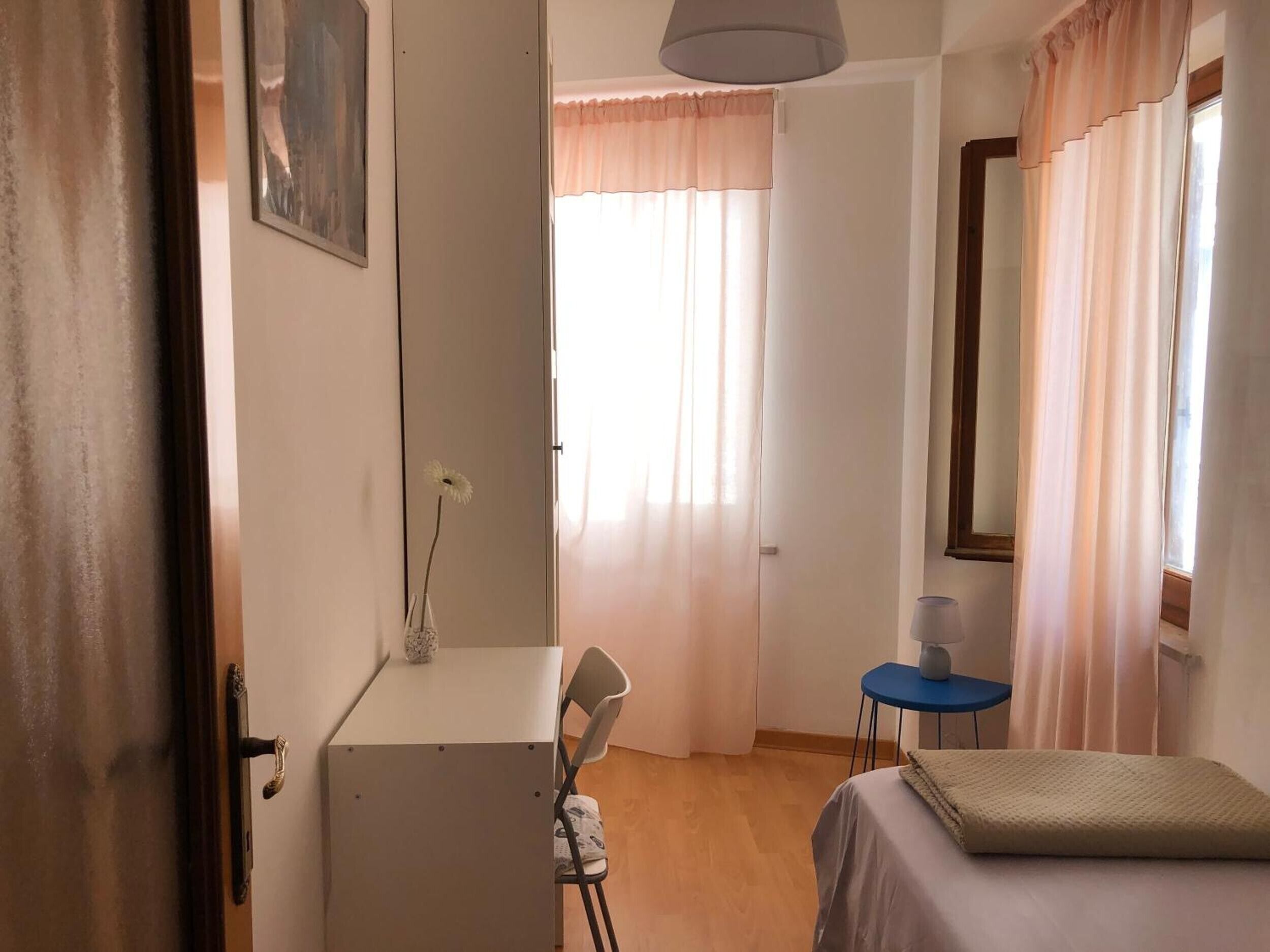 A bedroom with a bed, a desk, a chair, a lamp, and a window with curtains.