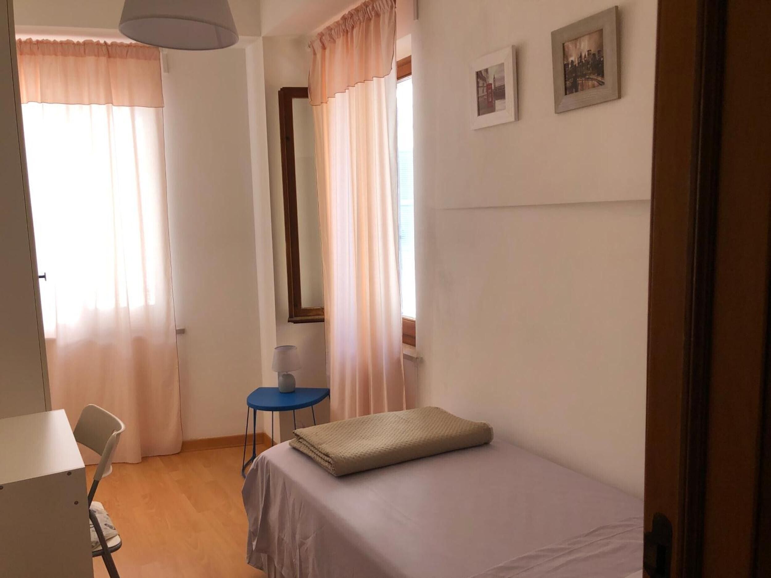 Ein Schlafzimmer mit Bett, Schreibtisch, Stuhl, Lampe und zwei mit Vorhängen versehenen Fenstern.