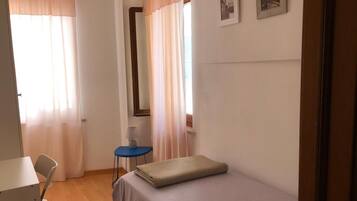 Ein Schlafzimmer mit Bett, Schreibtisch, Stuhl, Lampe und zwei mit Vorhängen versehenen Fenstern.
