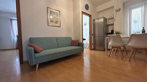Una sala de estar con sofá, un comedor con sillas, un refrigerador y un ventanal con cortinas.
