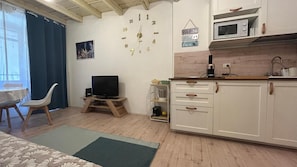 A compact living space with a kitchenette, a television, a dining area with a chair, and a clock on the wall. - Ankon Apartments Suite Don Gioia (Ancona)