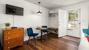 A room with a wooden dresser, two blue chairs, a small table, a TV mounted on the wall, and a door leading outside. - Jacobson's Cottages Cabin #3 (East Glacier Park)