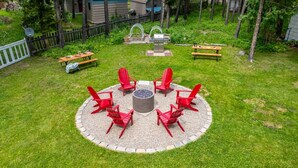 A circular outdoor seating area with red chairs and a central fire pit, surrounded by a gravel ring. - Jacobson's Cottages Cabin #3 (East Glacier Park)
