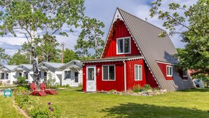 A red house with a sloped roof, surrounded by a well-maintained lawn and trees. - Jacobson's Cottages Cabin # 5 (East Glacier Park)