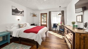 A bedroom with a bed, a desk, a chair, a window, and a door. - Jacobson's Cottages Cabin # 5 (East Glacier Park)