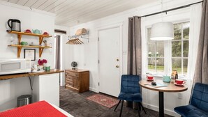 A compact kitchen with a microwave, tea set, and a small cabinet. There is a dining area with two chairs and a table, and a window with curtains. - Jacobson's Cottages Cabin #10 (East Glacier Park)