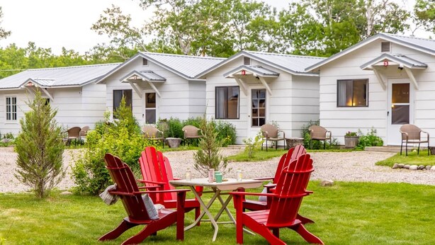 A row of white cabins with a gravel path and red Adirondack chairs in the foreground.