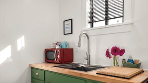A kitchen with a sink, a red microwave, and a window with blinds.