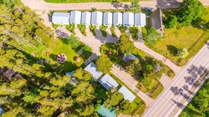 An aerial view of a property with multiple buildings, a parking lot, and surrounding greenery.