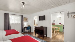 A bedroom with two beds, a desk, a chair, a TV, and a kitchenette.