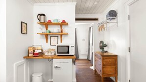A narrow hallway with a kitchenette area featuring a microwave, a small fridge, and a wooden shelf with kitchenware. - Jacobson's Cottages Cabin #11 (East Glacier Park)