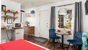 A compact room with a dining table, two chairs, a microwave, a small cabinet, and a window with curtains. - Jacobson's Cottages Cabin #11 (East Glacier Park)