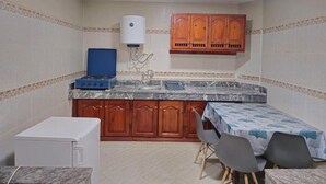 Eine kleine Küche mit Gasherd, Spüle, Holzschränken, einem Tisch mit Stühlen und einer Deckenleuchte.