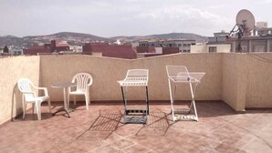 Eine Dachterrasse mit Blick auf ferne Hügel, weißen Kunststoffstühlen und einem Metalltisch.