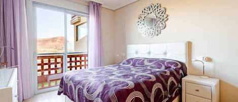 A bedroom with a bed, a nightstand, a mirror, and a sliding door to a balcony.