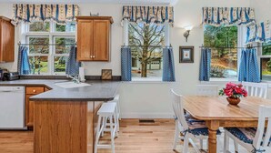 Een keuken met houten kasten, een granieten aanrecht, een spoelbak en een eethoek met een houten tafel en witte stoelen.