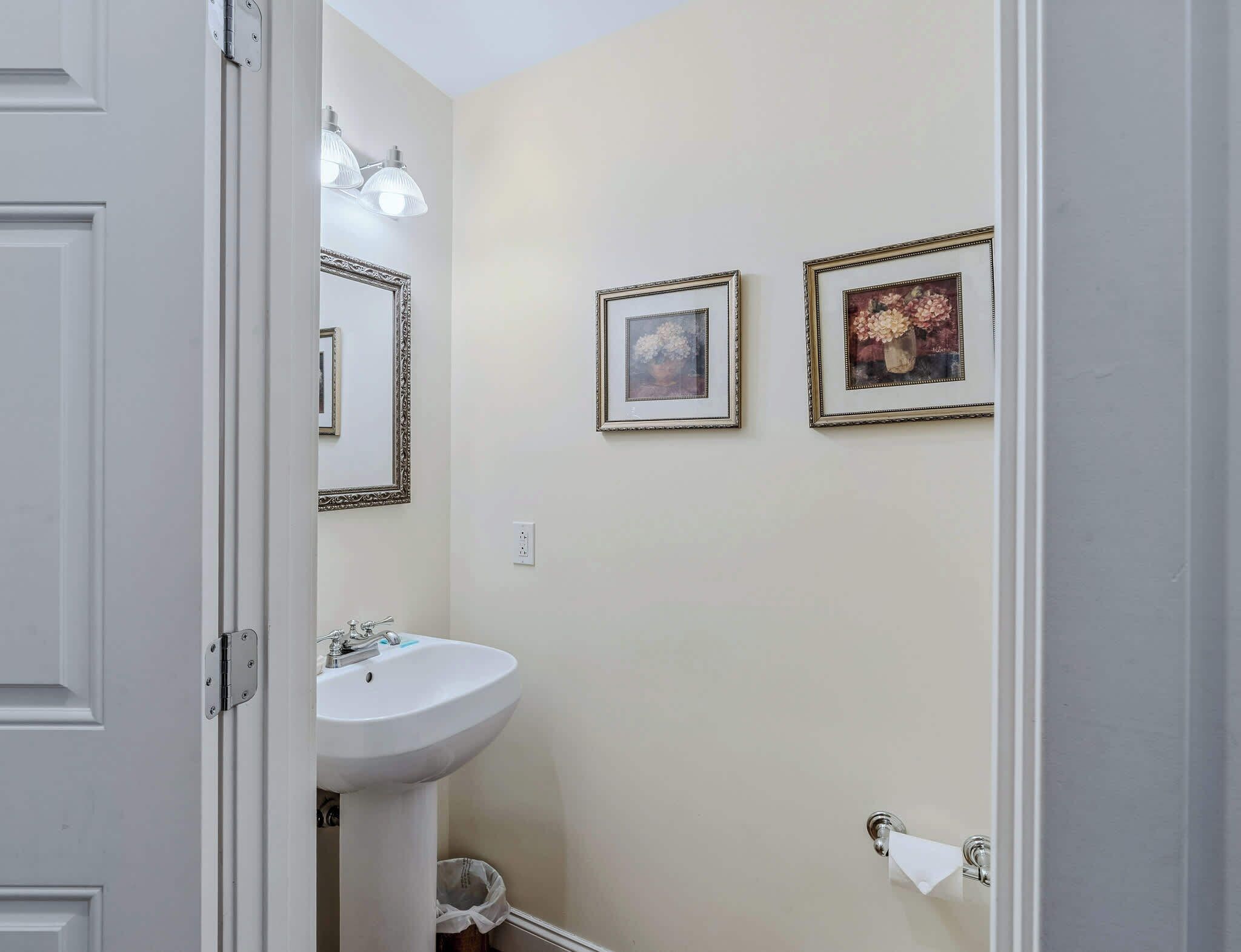 A bathroom with a white sink, two framed pictures on the wall, and a mirror above the sink.