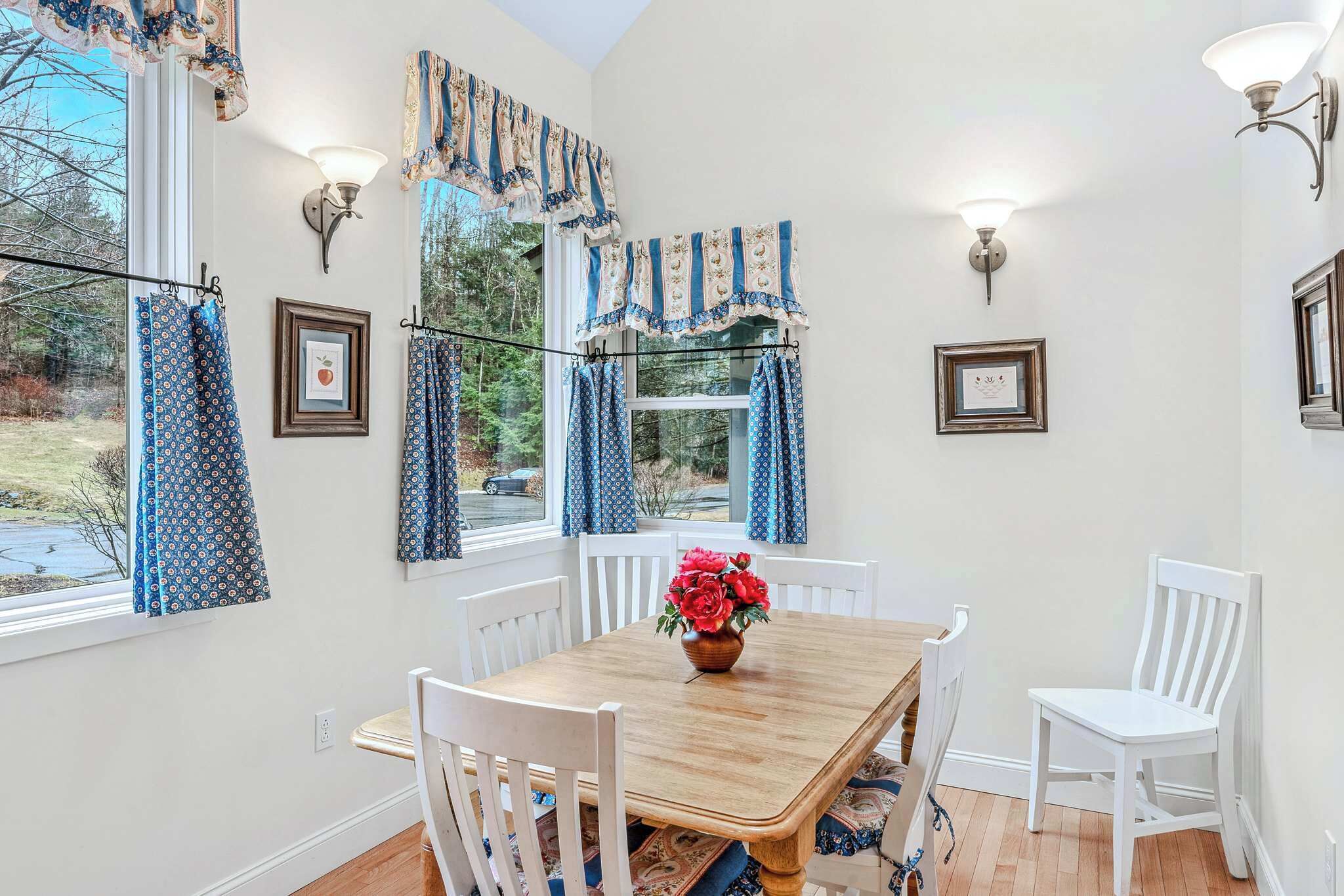 A dining area with a wooden table, white chairs, blue patterned curtains, and wall-mounted light fixtures.