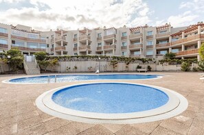 A hotel with a swimming pool area, multiple balconies, and a clear sky.