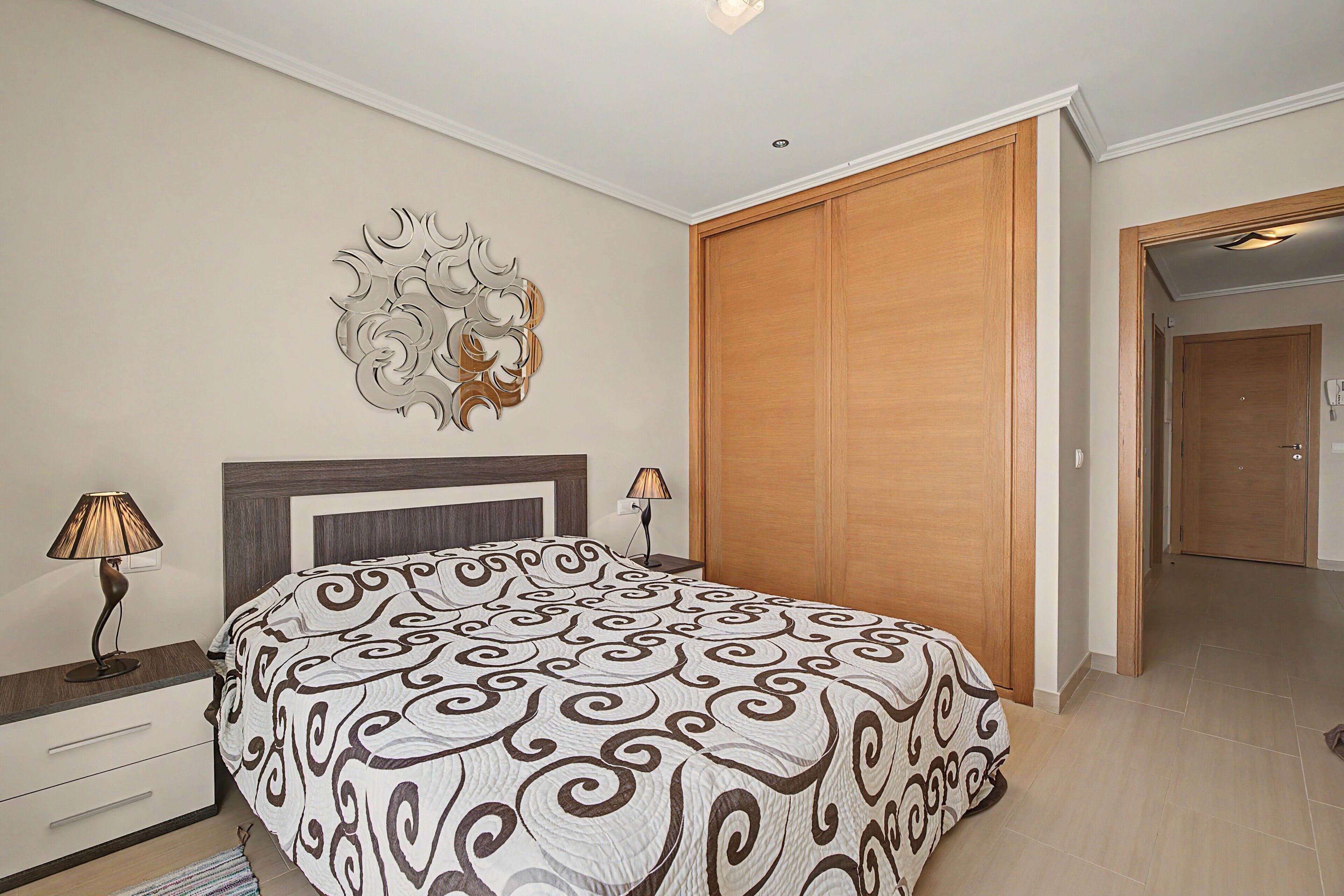 Un dormitorio con una cama, lámparas de noche, un adorno de pared y un armario.