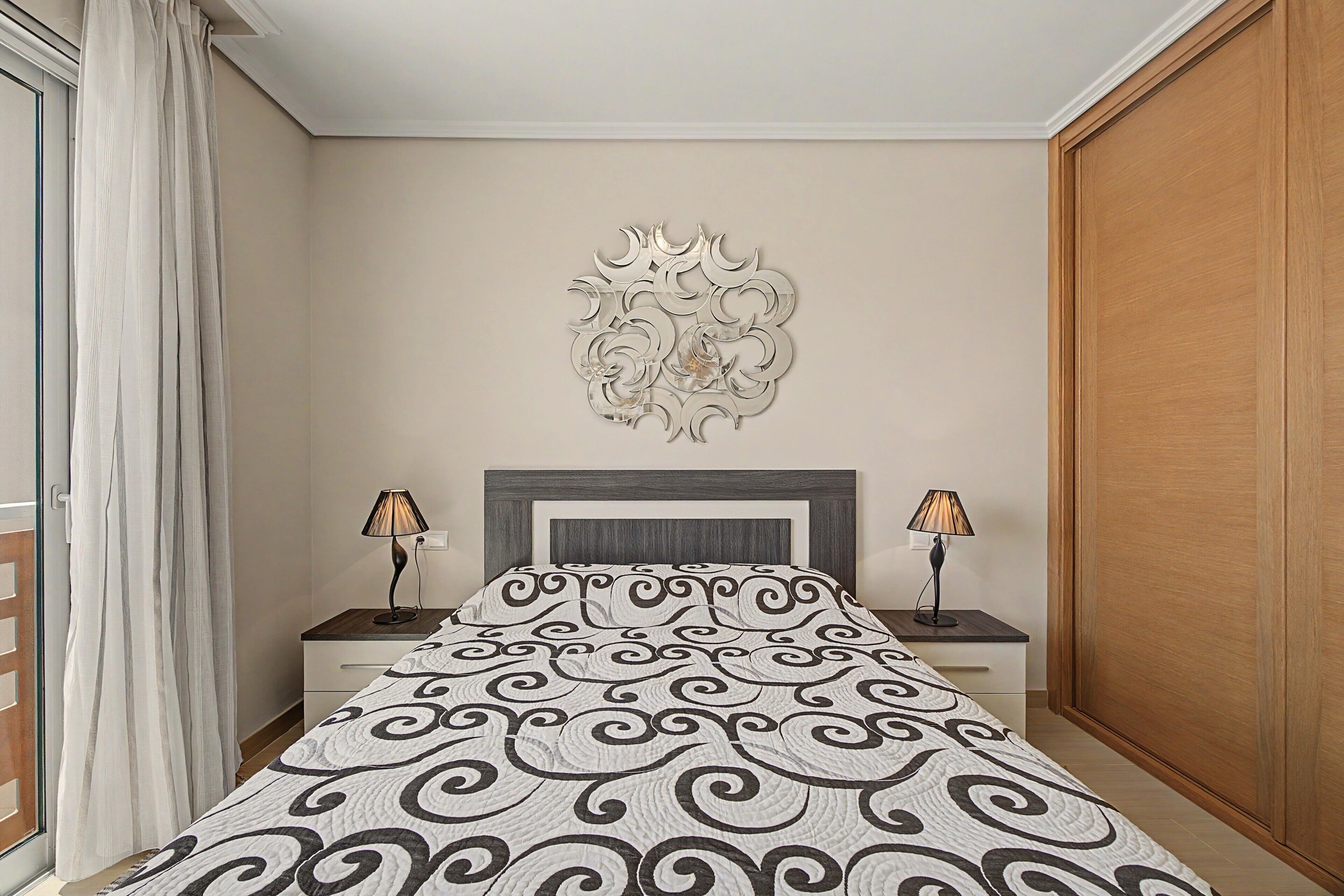 A bedroom with a bed, two bedside tables, a decorative wall piece, and a wooden wardrobe.