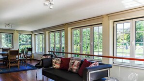 A room with a black sofa, multiple windows, a dining table with chairs, and a fan. - QUINTA DO MOSTEIRO:Charming refuge between history and nature (Ponte da Barca)
