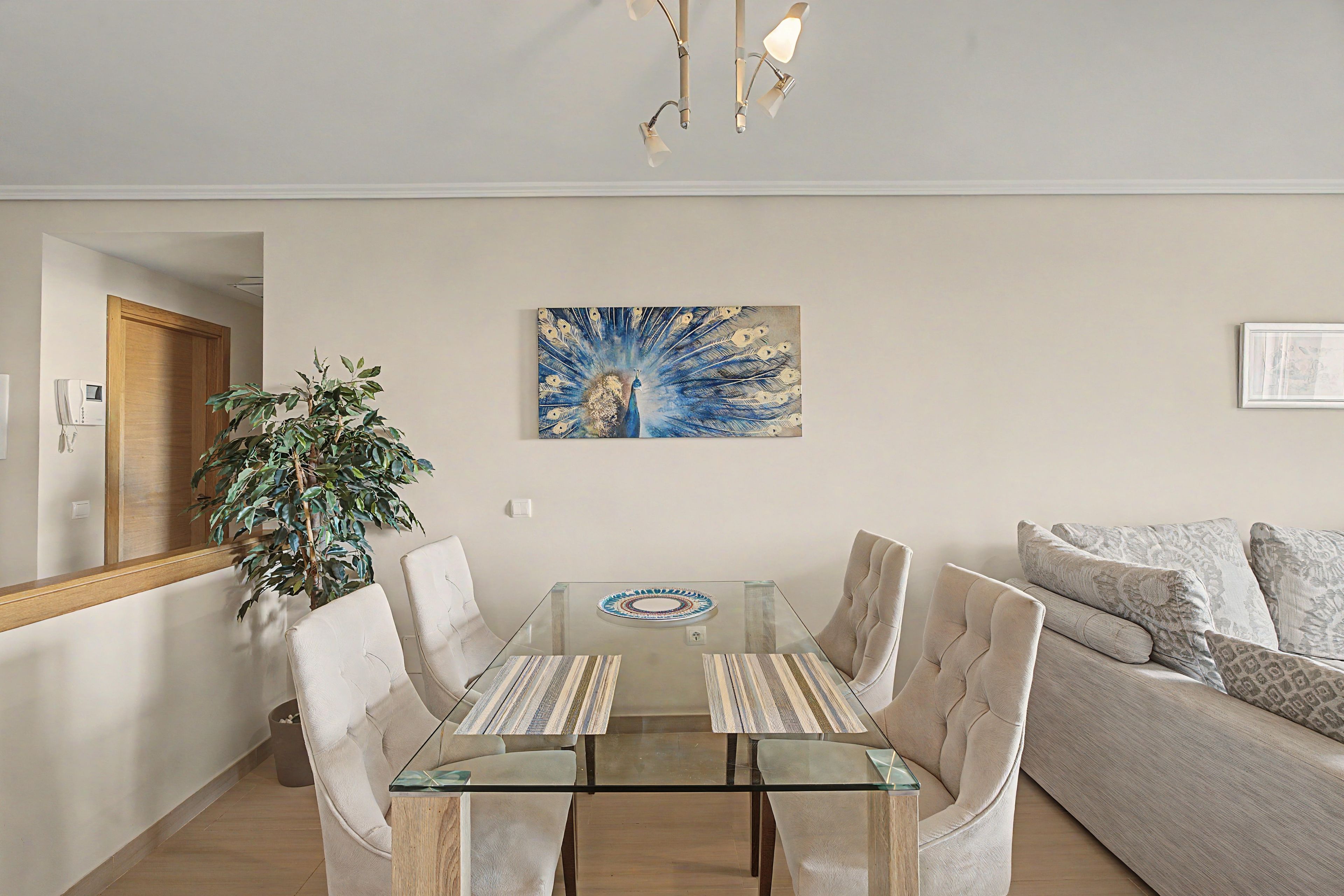 Een moderne woonkamer met een glazen eettafel, beige banken en een groot schilderij aan de muur.