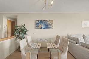 A modern living room with a glass dining table, beige sofas, and a large painting on the wall.