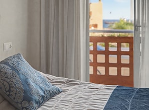 A bed with a patterned pillow, a view of the outdoors through a window, and a door with a grid pattern.