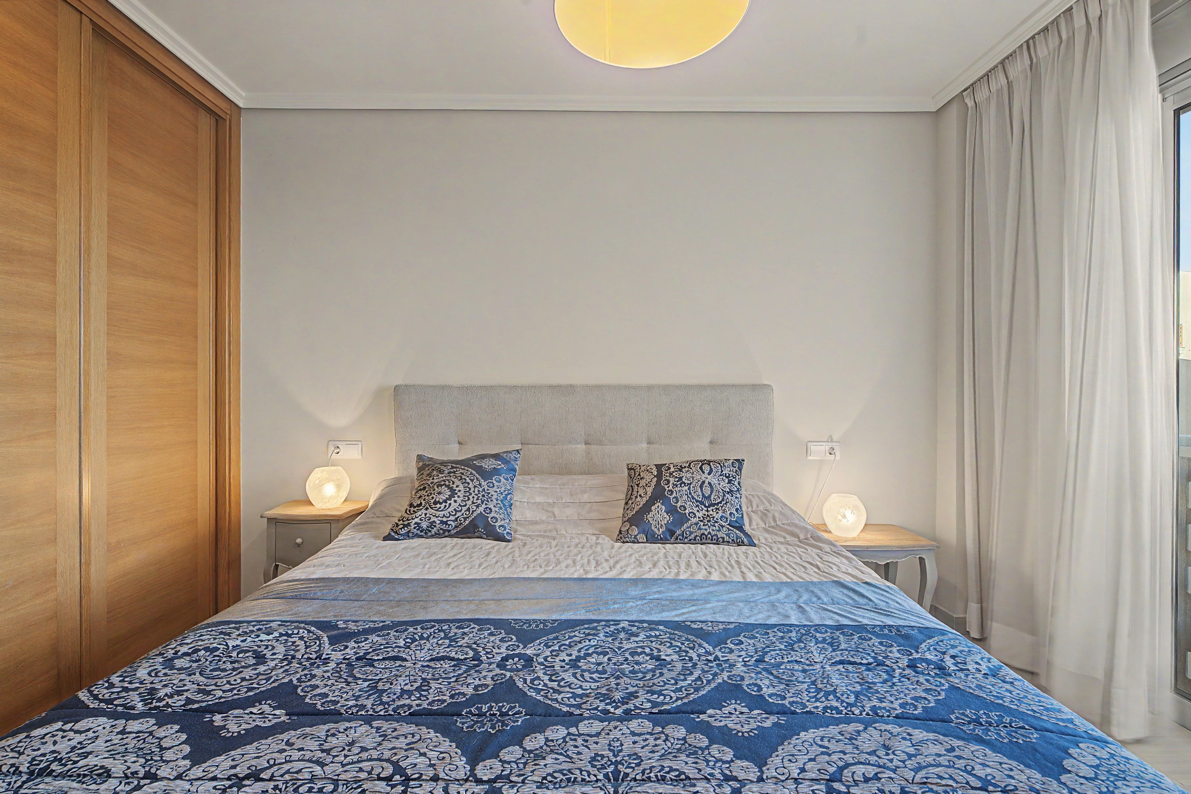 A bedroom with a bed, two bedside lamps, a nightstand, and a window with curtains.
