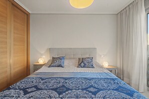 A bedroom with a bed, two bedside lamps, a nightstand, and a window with curtains.