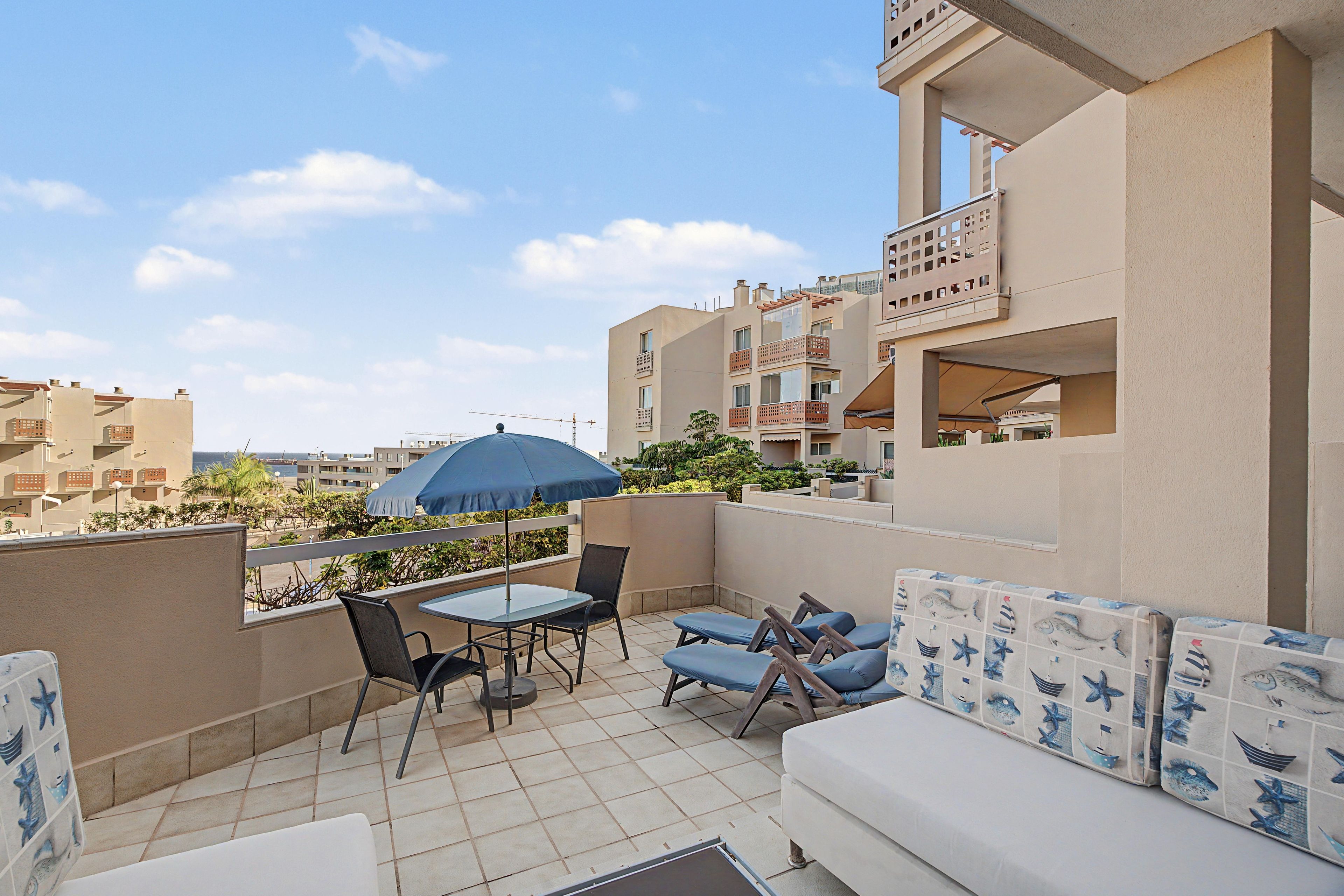 A rooftop terrace with a table, chairs, a blue umbrella, and a sofa with a nautical theme.
