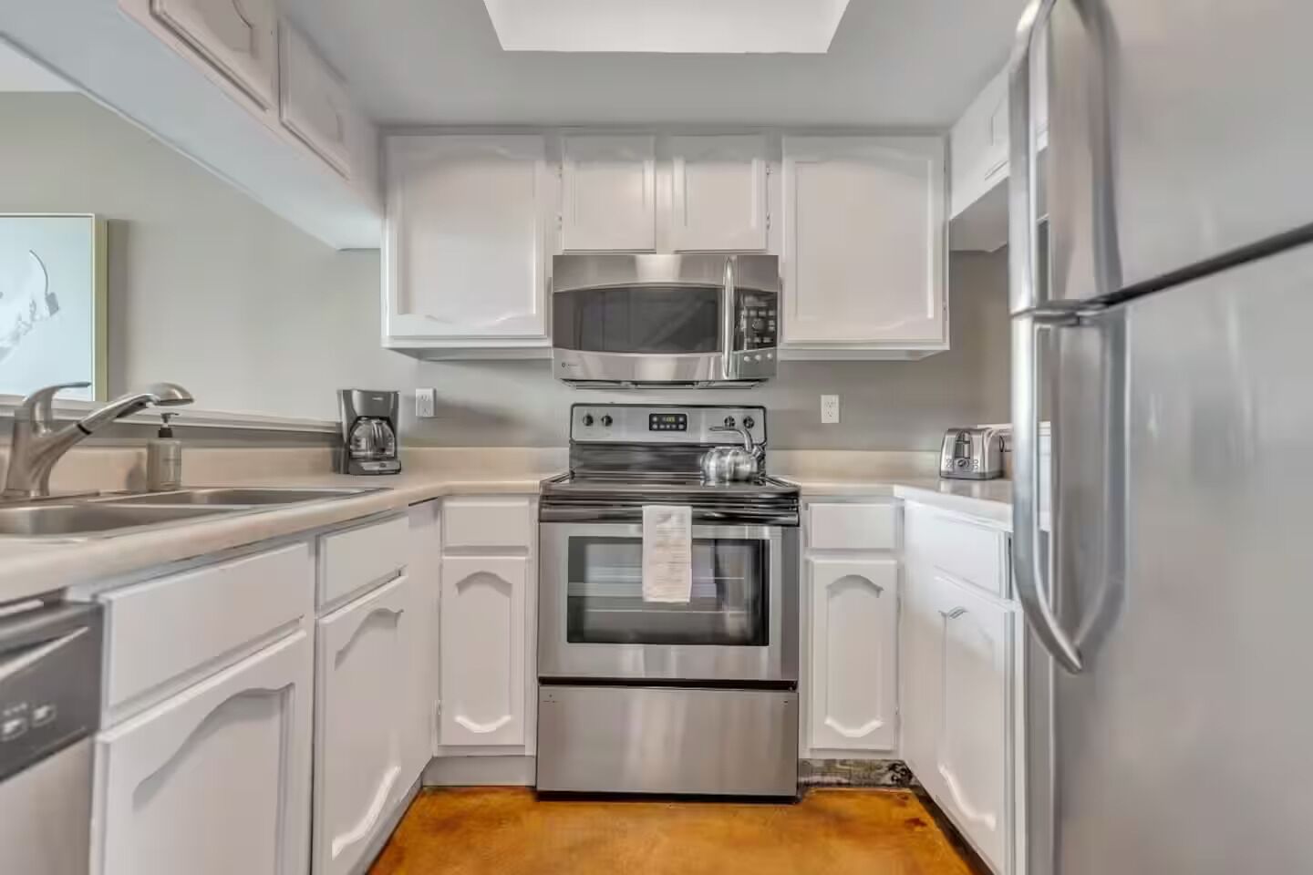 A modern kitchen with white cabinets, stainless steel appliances, and a wooden floor.