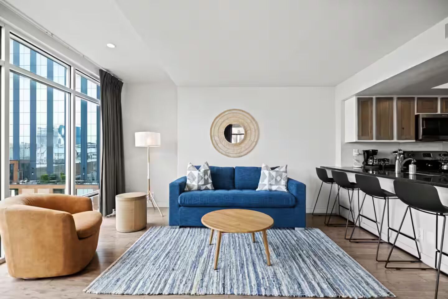 A modern living room with a blue sofa, a round coffee table, and a view of the city through large windows.