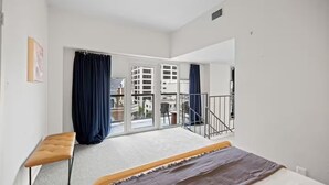 A bedroom with a bed, a bench, a large window, and a balcony. - Top Floor 2BR Penthouse - Great for Big Groups (Austin)