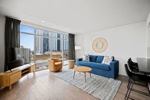 Un salon moderne doté d’une grande fenêtre, d’un canapé bleu, d’une table basse en bois, d’un téléviseur et d’un coin repas.
