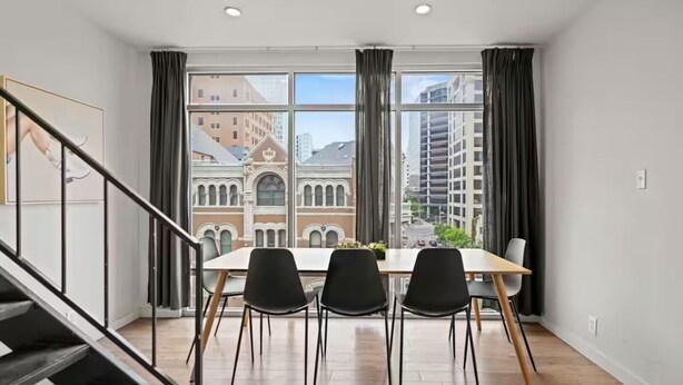 A dining area with a table and chairs, large windows with curtains, and a staircase. - Top Floor 2BR Penthouse - Great for Big Groups (Austin)