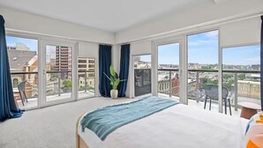 A hotel room with a large bed, a potted plant, and a balcony with a view of the city. - Top Floor 2BR Penthouse - Great for Big Groups (Austin)