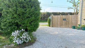 A gravel driveway leading to a wooden gate, surrounded by greenery and potted plants. - Gite Barton 6 persons 500m from Utah Beach (Sainte-Marie-du-Mont)