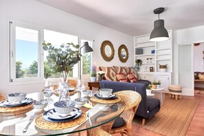 Ein Essbereich mit einem Glastisch, Korbstühlen und einem blauen Sofa.