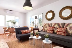 Ein modernes Wohnzimmer mit einer Couch, zwei runden Spiegeln und einem Essbereich mit Korbmöbeln.