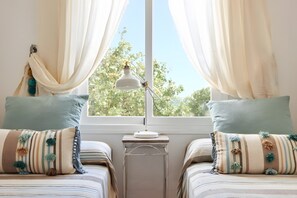 Ein Schlafzimmer mit zwei Betten, einem Nachttisch, einer Lampe und einem Fenster mit Vorhängen.