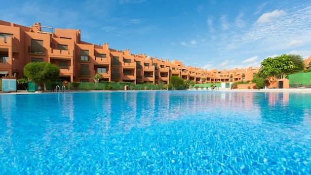 A swimming pool with clear blue water, surrounded by a row of multi-story buildings with balconies.